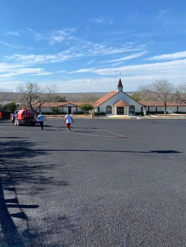 New asphalt parking lot with two people walking toward a church under a blue sky.