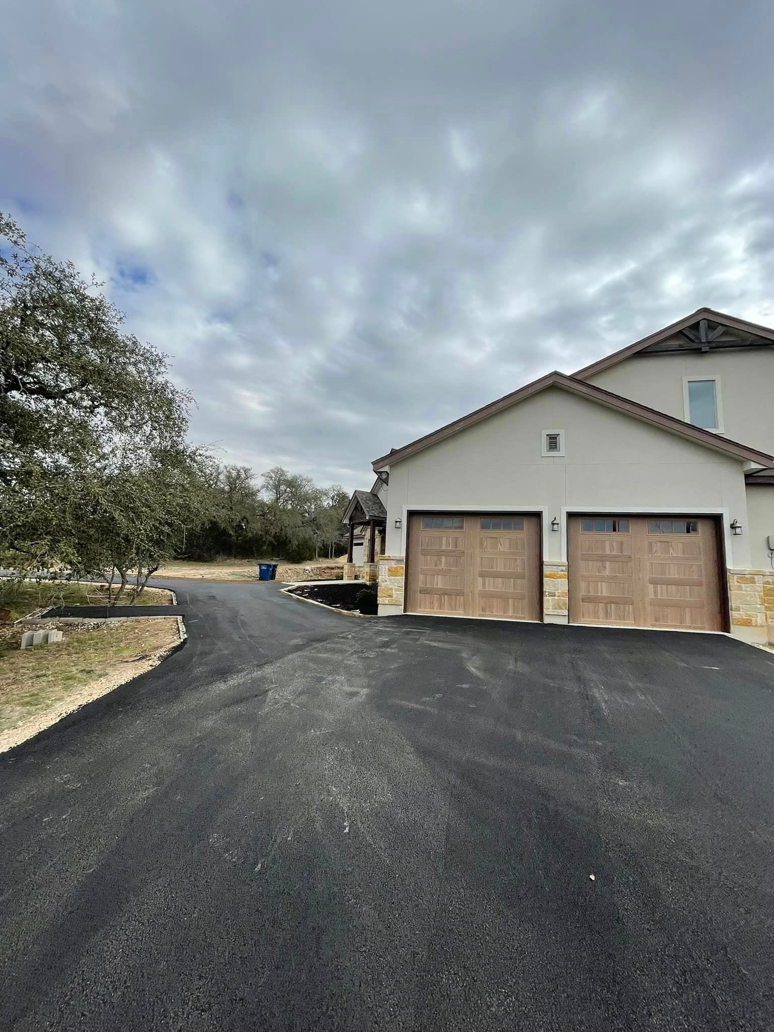 Paved driveway leading to a two-car garage with brown doors, set against a cloudy sky.