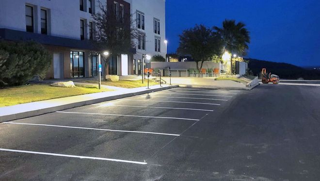 Exterior view of a building at dusk, with lit parking spaces and bike racks in the foreground.