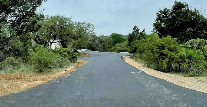 Asphalt road curving through a green, tree-filled landscape.