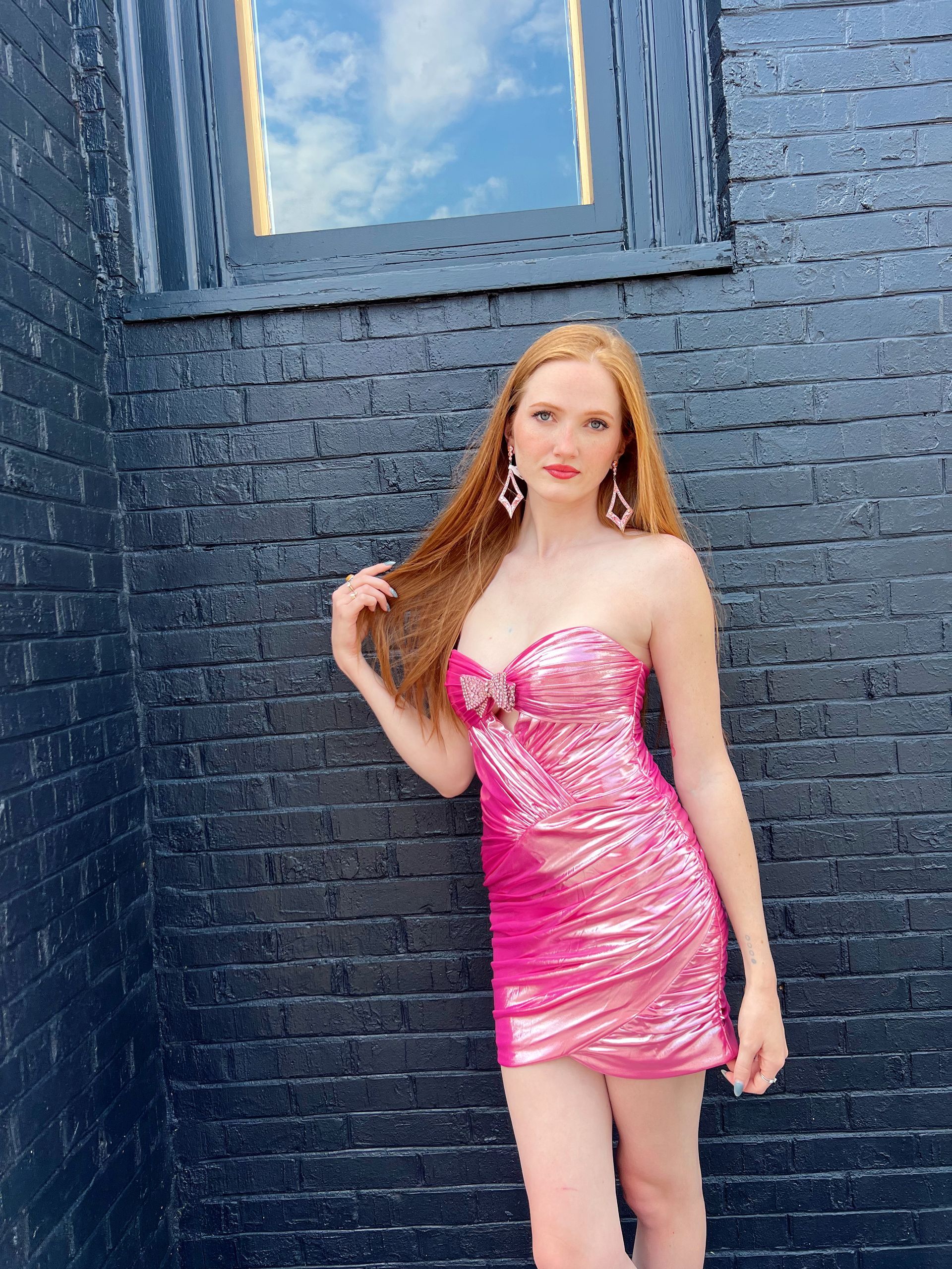 Woman in a pink, sparkly strapless dress, leaning against a dark brick wall