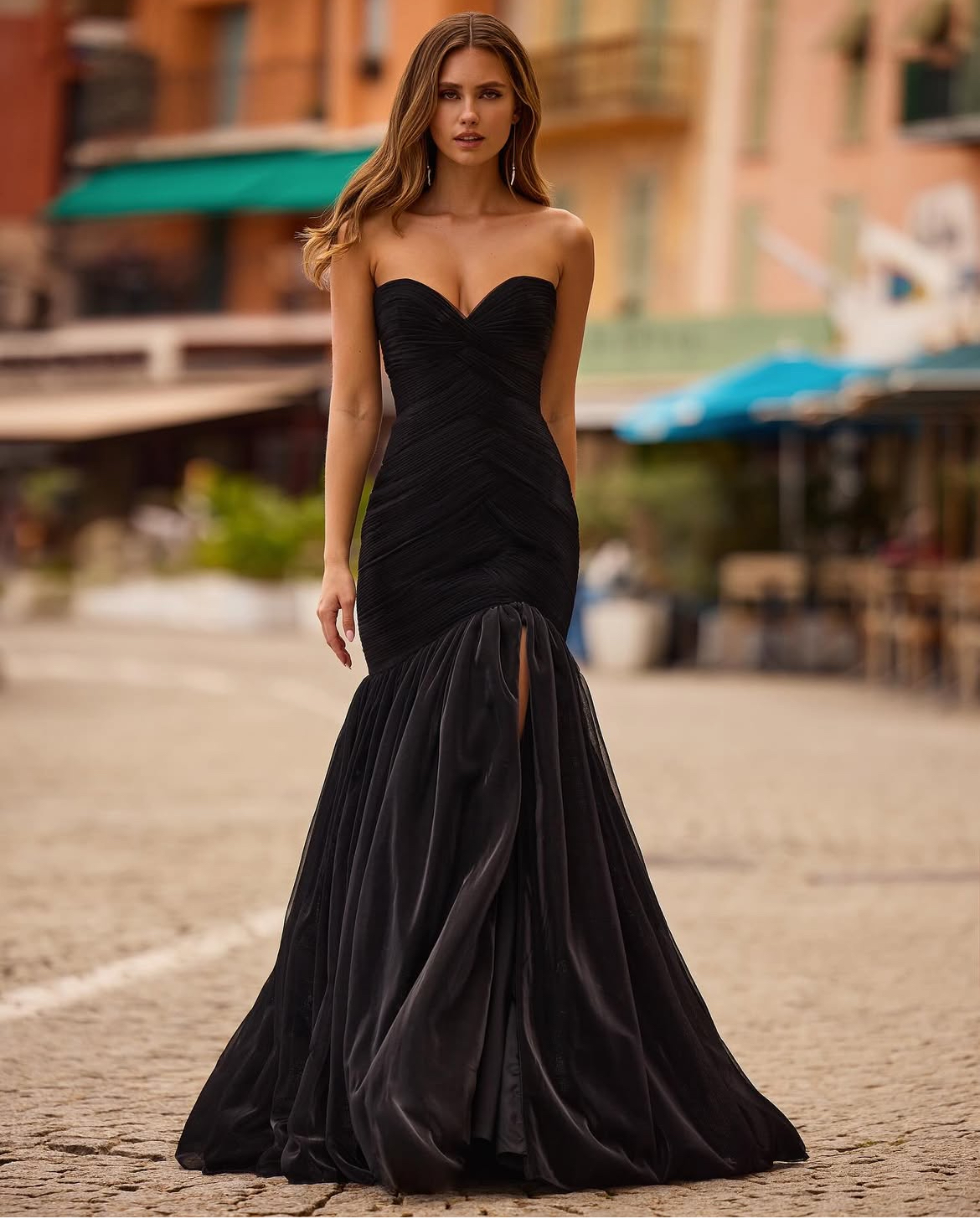 Woman in black strapless gown with fishtail hemline, posing on cobblestone street