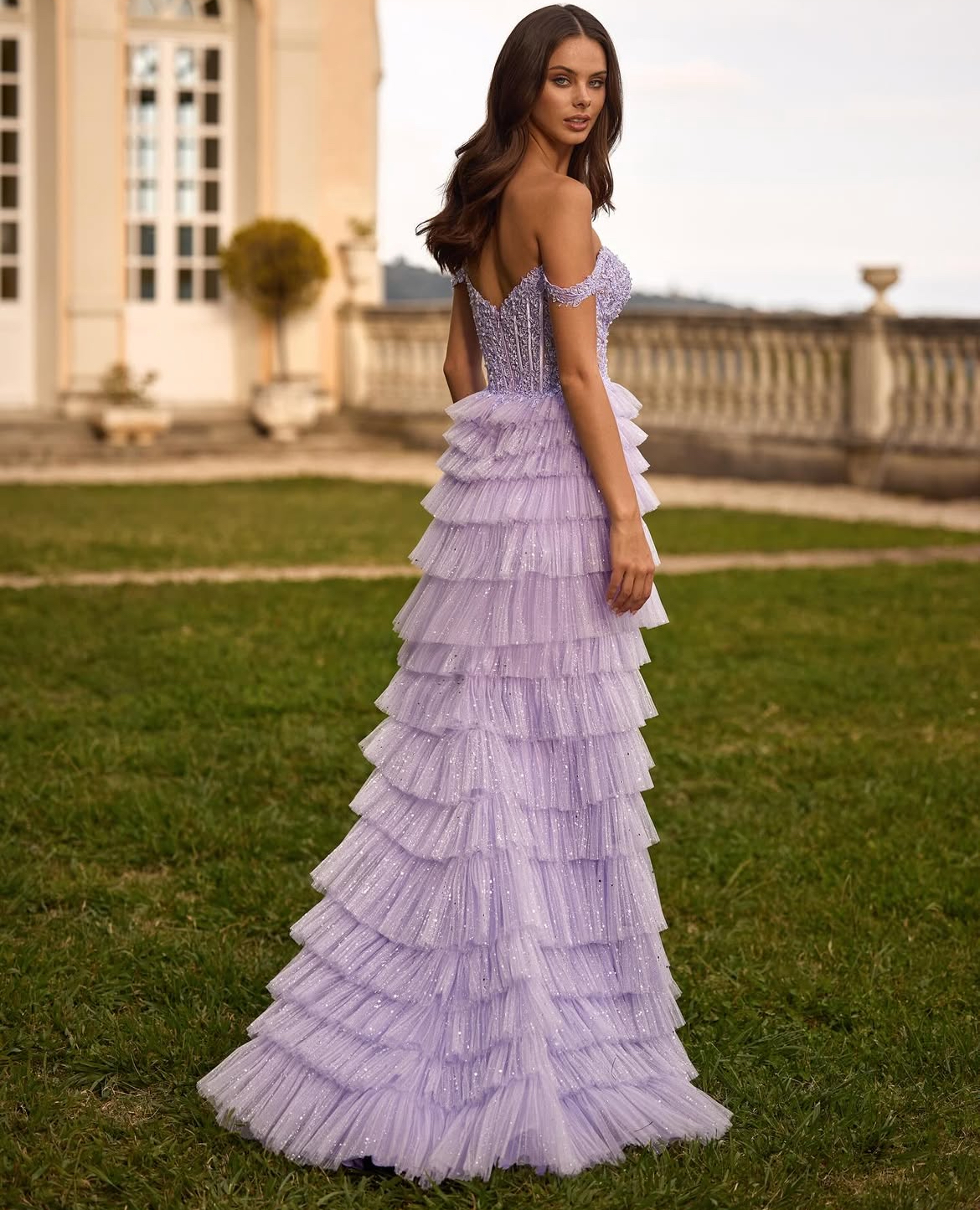 Woman in a lavender ruffled gown poses outdoors, looking over shoulder
