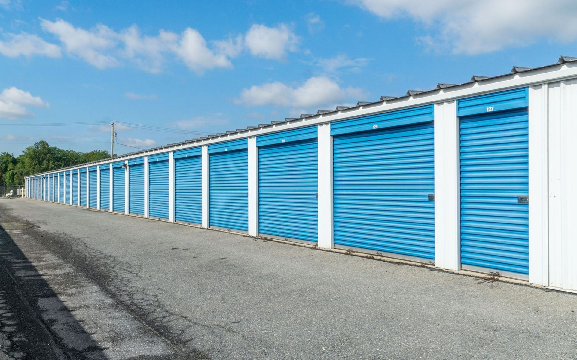Row of blue storage unit doors along a gravel path, under a blue sky.
