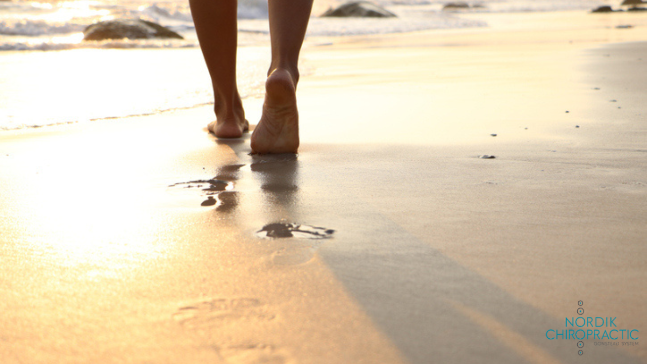 Bare feet walking on a sunlit beach, leaving footprints in wet sand at sunset