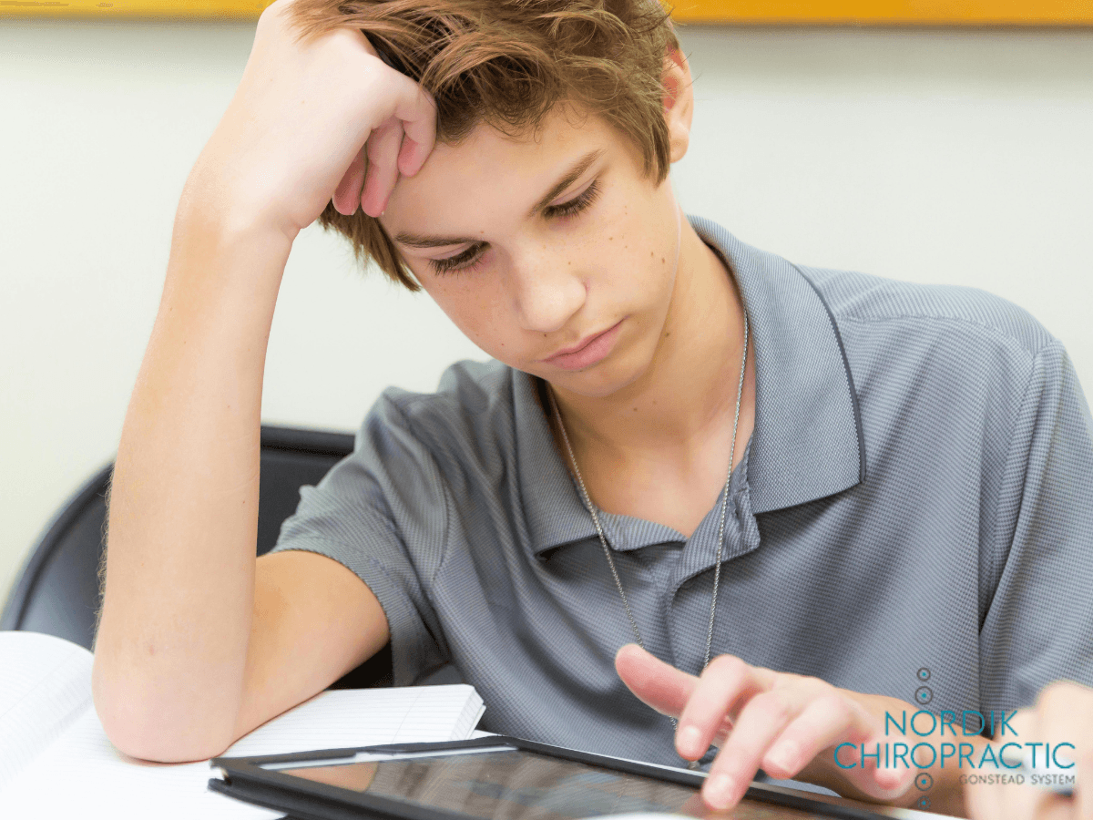 Person studying at a table, head resting on hand, looking at a tablet with papers nearby.