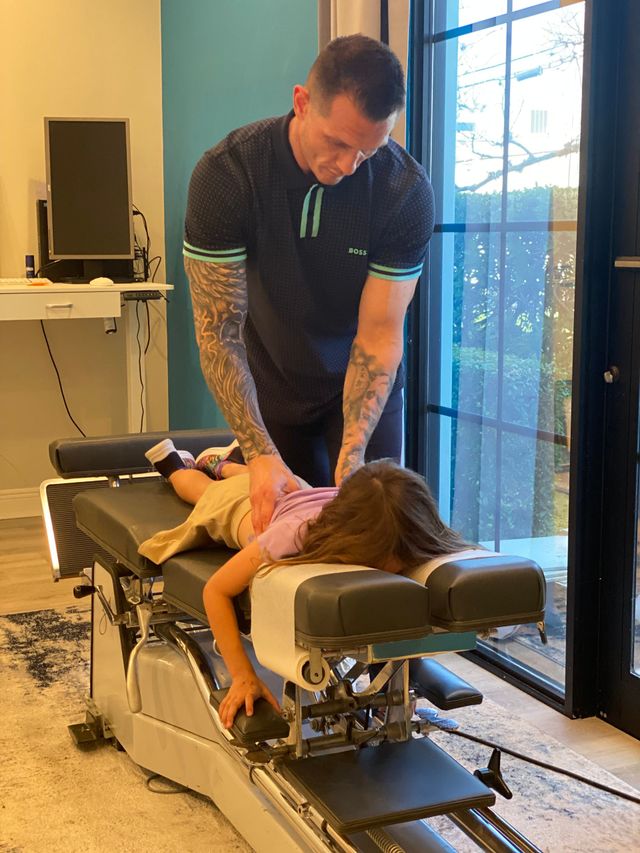 Massage therapist pressing on client lying face down on a treatment table in a bright room