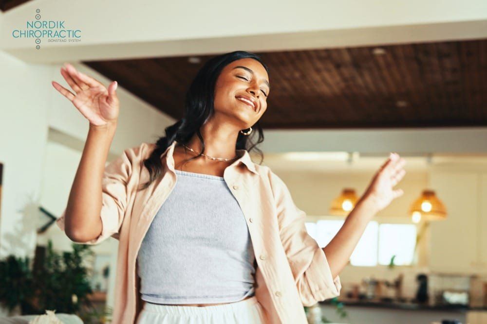 Smiling woman dancing in a bright modern room, wearing a beige shirt and white top