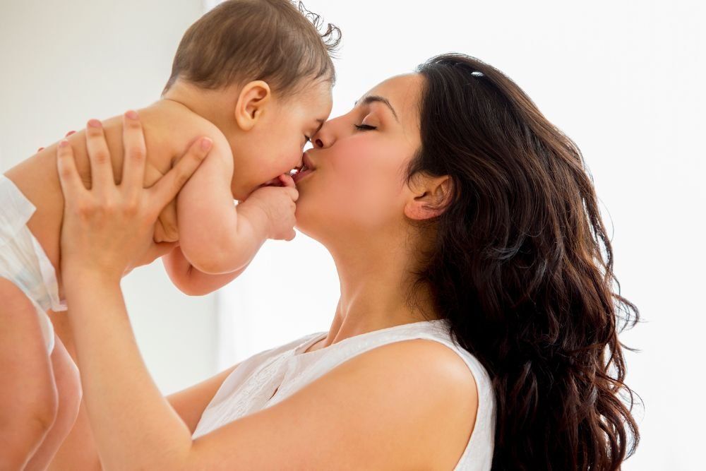 Mother kissing baby on the nose against a white background