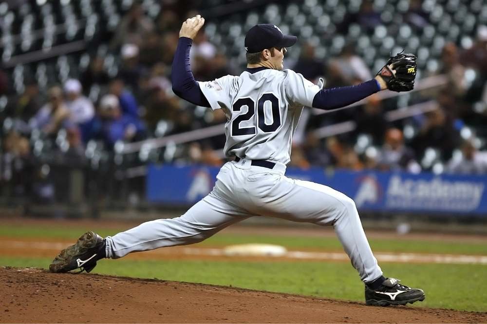 Baseball pitcher in white uniform mid-throw on the mound during a game