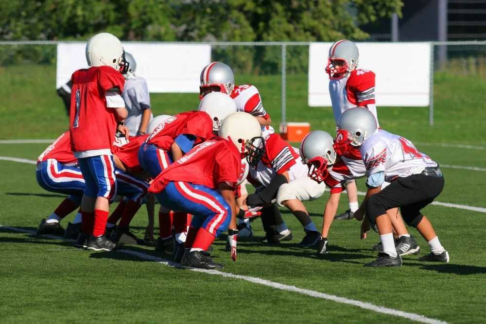 Youth football teams lined up at the line of scrimmage on a grassy field, ready for the snap.