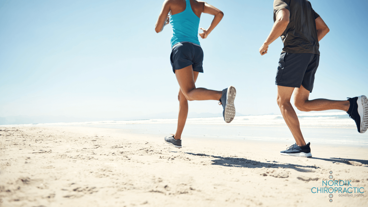 Two people jogging on a sunny beach, seen from behind.
