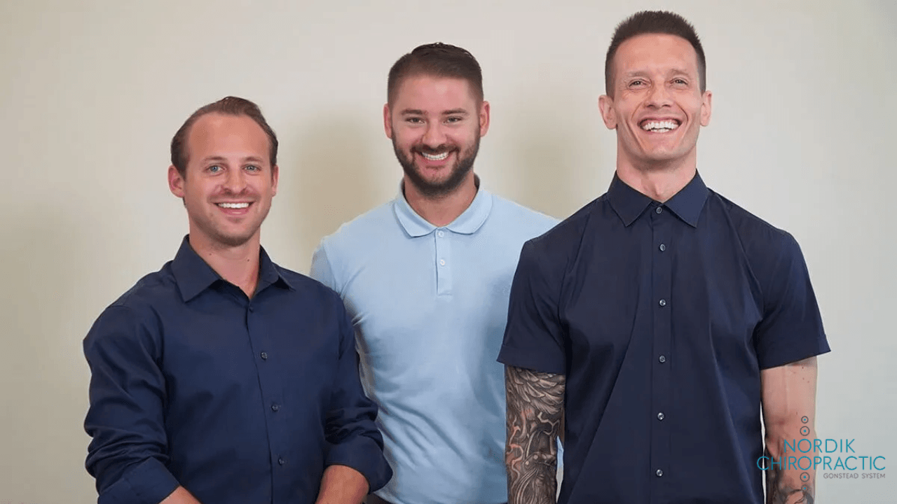 Three smiling people standing indoors, wearing collared shirts against a plain background