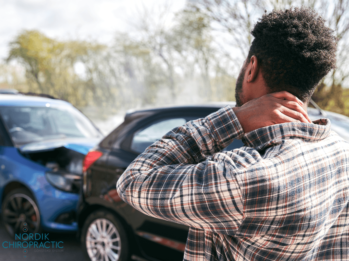 Man rubbing the back of his neck beside parked cars in a sunny parking lot