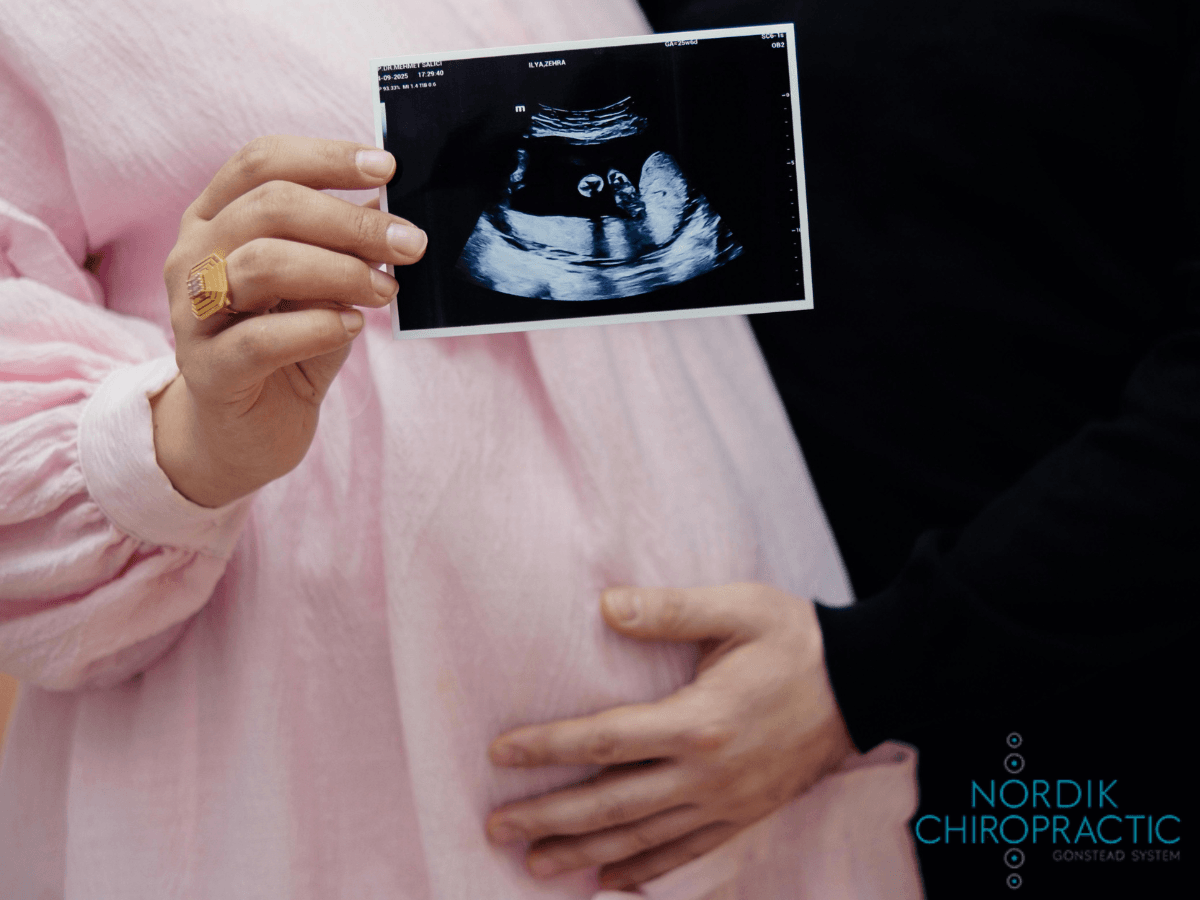 Pregnant person holding an ultrasound print beside another person, with hands resting on the belly.