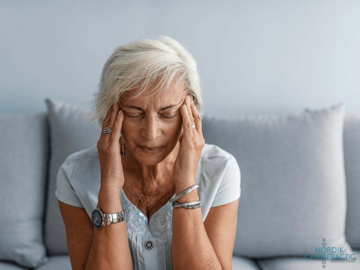 Woman sitting on a sofa, holding her temples with eyes closed, looking stressed or in pain