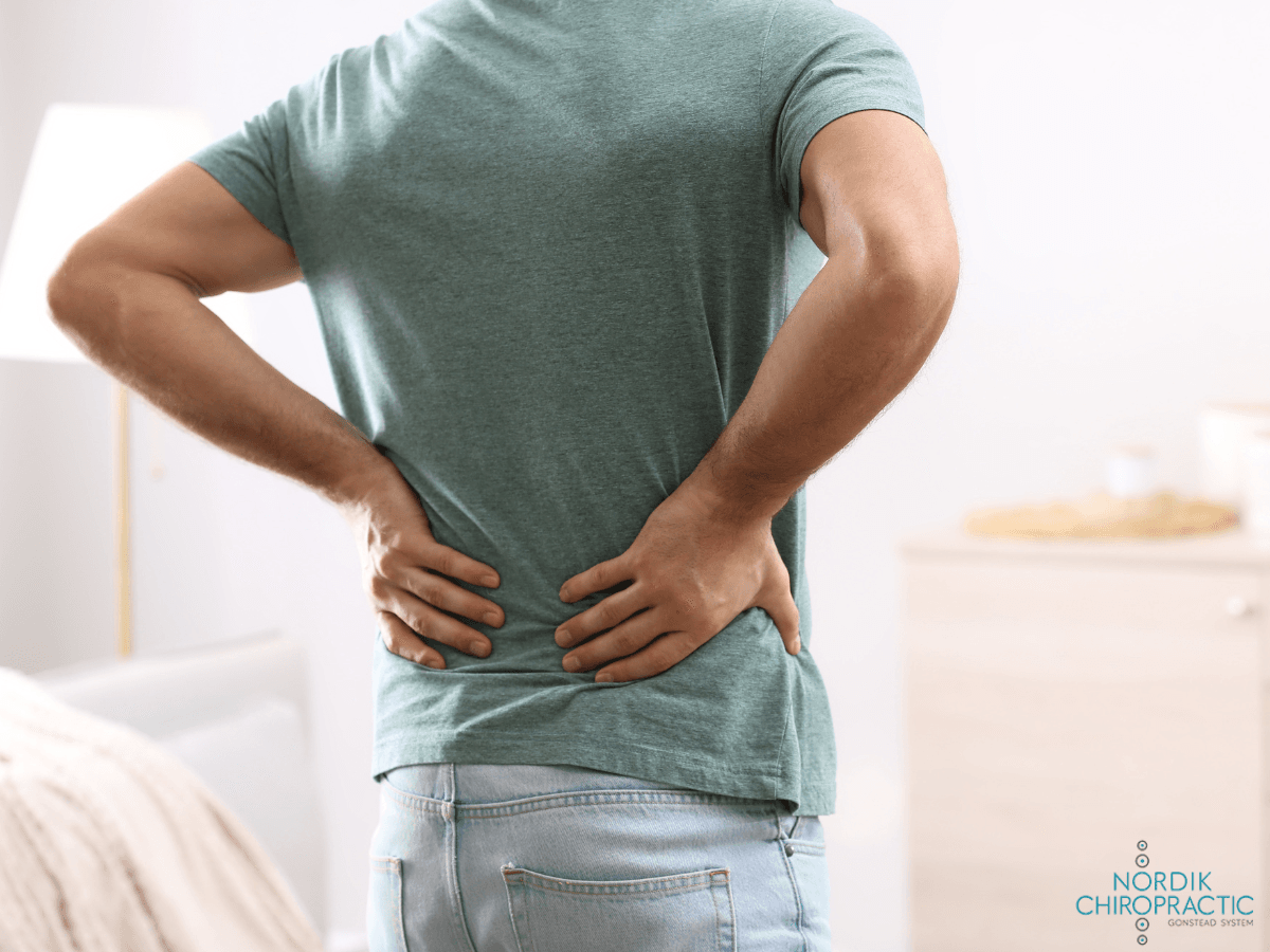 Person holding lower back while standing in a bedroom, suggesting back pain