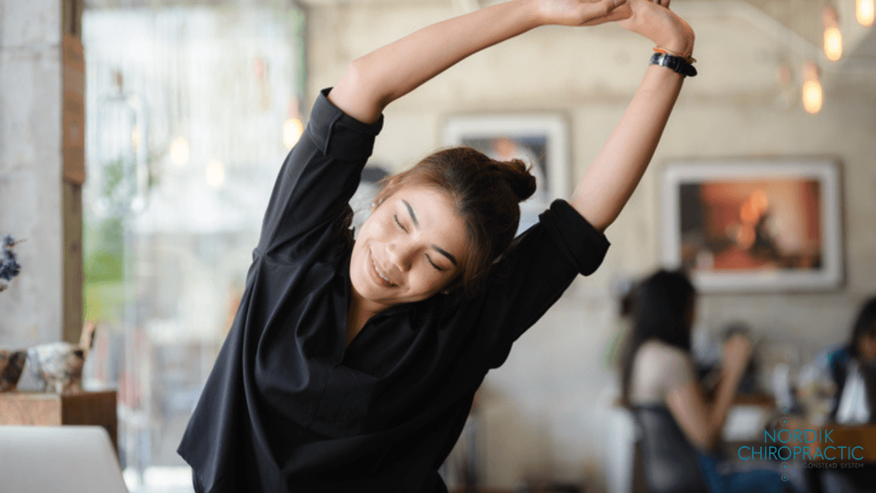 Smiling person stretching with arms overhead in a bright café or coworking space