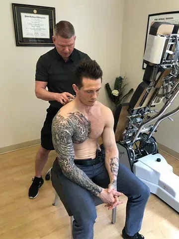 Man receiving neck treatment while seated, with therapist standing behind in a clinic room.