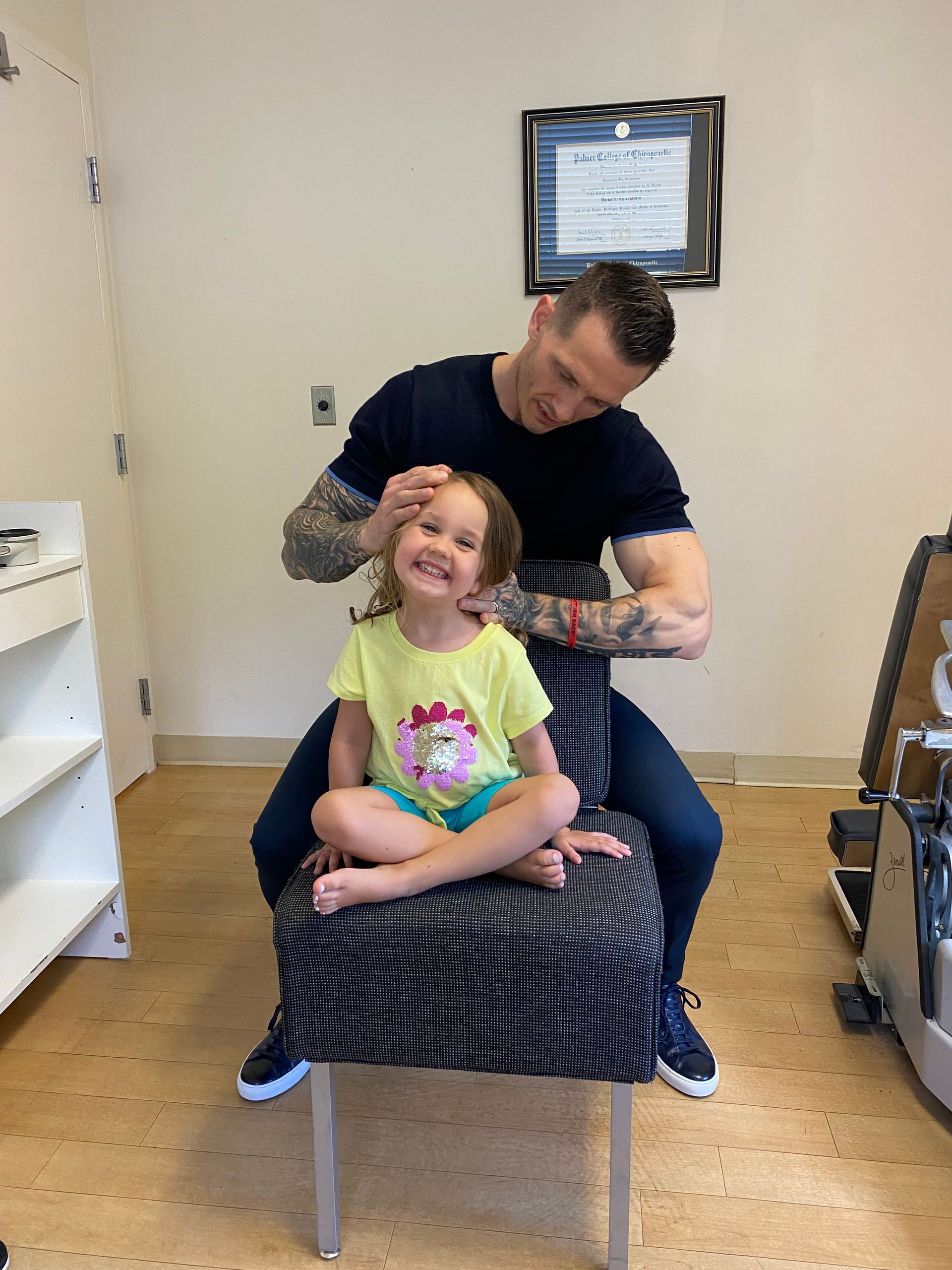 Man styling a child’s hair in a salon chair, both smiling in a bright room.