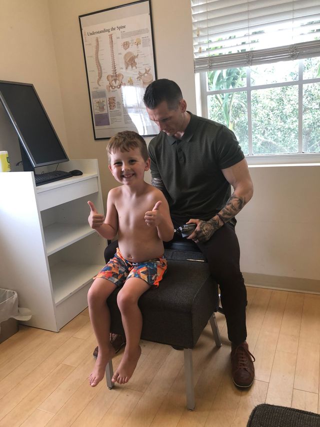 Child sitting on a man’s lap in a bright room, smiling and giving two thumbs up.