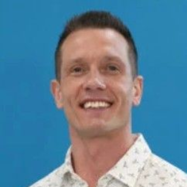 Smiling man in a white patterned shirt against a blue background