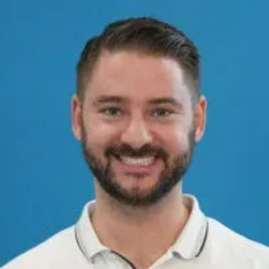 Smiling bearded man in a white polo against a blue background