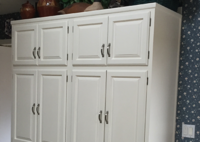 White kitchen cabinet with eight doors, metal handles, set against patterned wallpaper.
