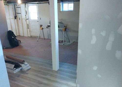 Basement renovation: partially finished room with exposed framing, drywall, flooring, and tools.
