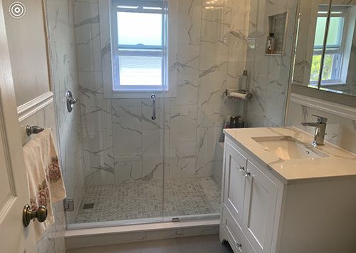 Bathroom with white marble tile shower, glass door, white vanity, and small window.