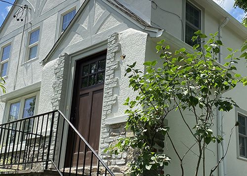 Two-story Tudor style house with brown door, white stucco walls, and stone accents.