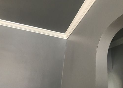 Gray walls with white crown molding meeting at a corner and an arched doorway.