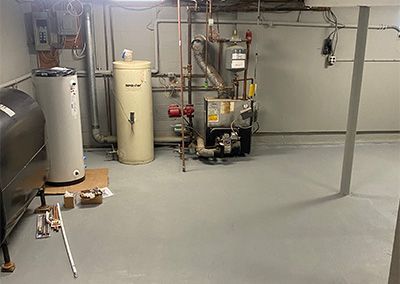 Basement utility room with heating and water systems: oil tank, water heater, furnace, gray painted floor.