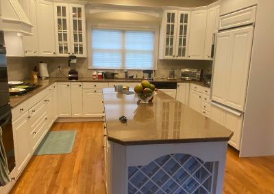 White kitchen with wooden floors and an island; countertops hold fruit and appliances.