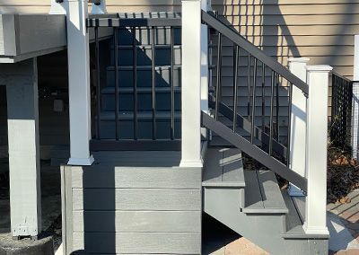 Gray wooden staircase with black railing and white posts, leading up to a deck.
