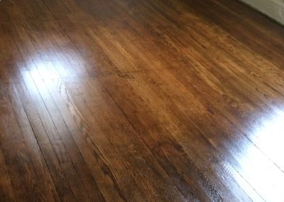 Shiny, brown wood-grain floor with streaks and highlights from natural light.