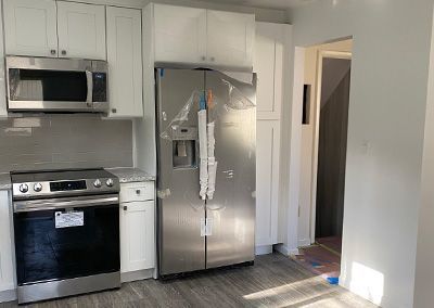 Newly renovated kitchen with white cabinets, stainless steel appliances, and a gray backsplash.