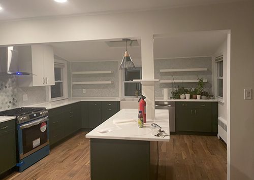 Newly renovated kitchen with dark green cabinets, white countertops, and wood floors.