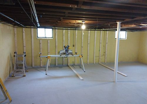Basement under construction. Yellow walls, wood framing, a miter saw, support beams, and a window.