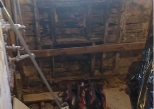 Exposed wooden ceiling beams in a room, with pipes and debris visible.