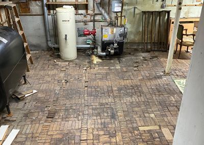 Basement with worn brick flooring, furnace, and water heater; walls have exposed wood beams.