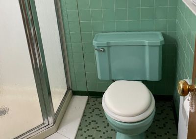 A green toilet with a matching tank in a bathroom with green tiled walls and a shower.