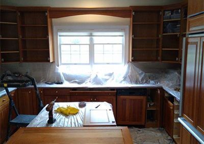 Kitchen cabinets with open doors, plastic sheeting, and tools on counters.