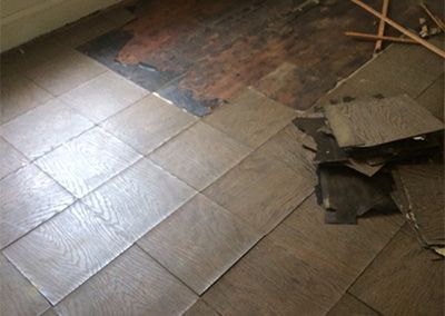 Damaged wood flooring with loose tiles and exposed subfloor.