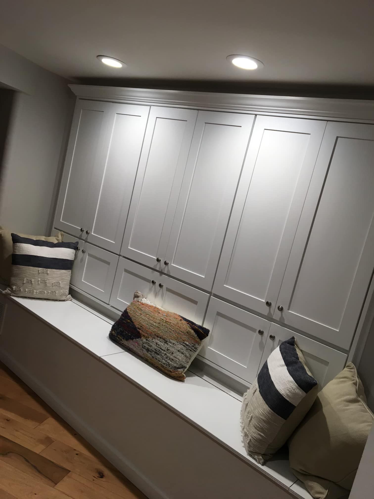 Built-in bench with grey cabinets above, lit by recessed lights. Pillows in neutral tones.