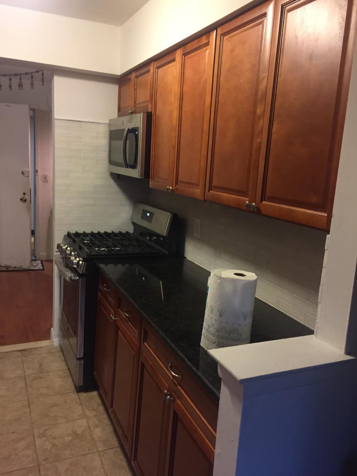 Kitchen with dark cabinets, black countertop, stainless steel appliances, and a paper towel roll.