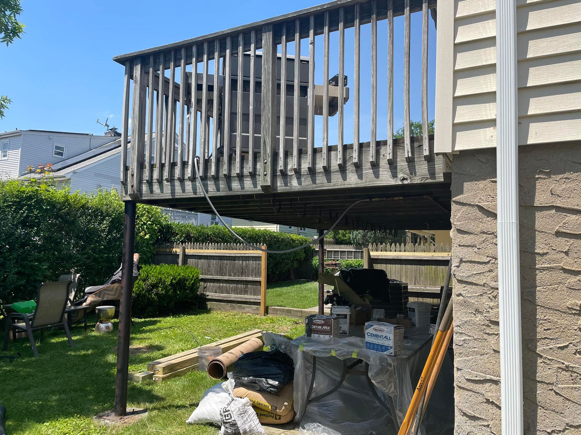 Exterior view of a weathered wooden deck supported by dark metal poles, with a cluttered yard below.