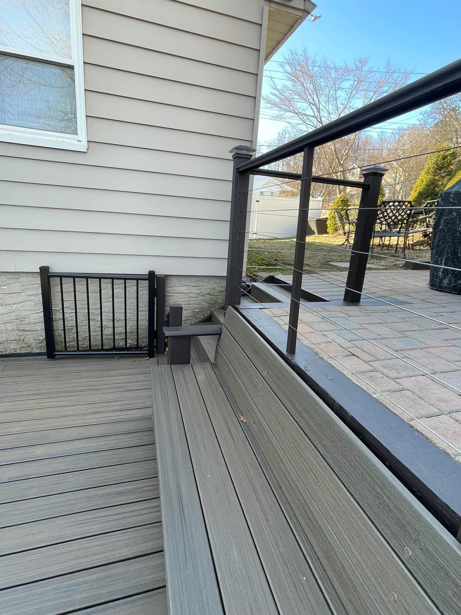 Wooden deck with black railings and a gate next to a house with gray siding.