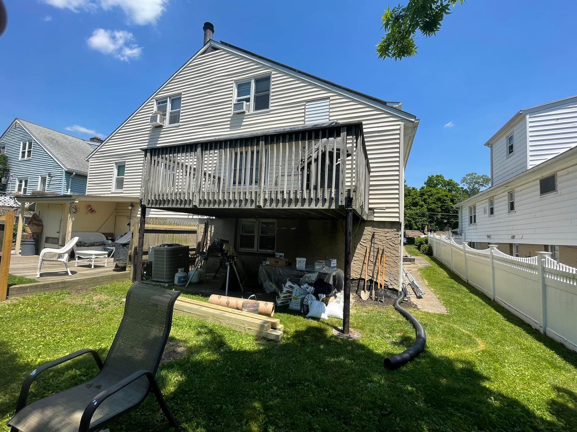 Backyard view of a two-story house with a wooden deck; various construction materials sit below.