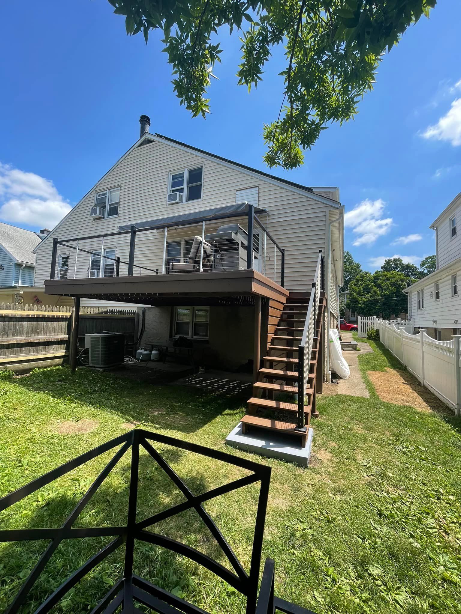 Backyard view of a two-story white house with a deck, stairs, and a grassy lawn on a sunny day.